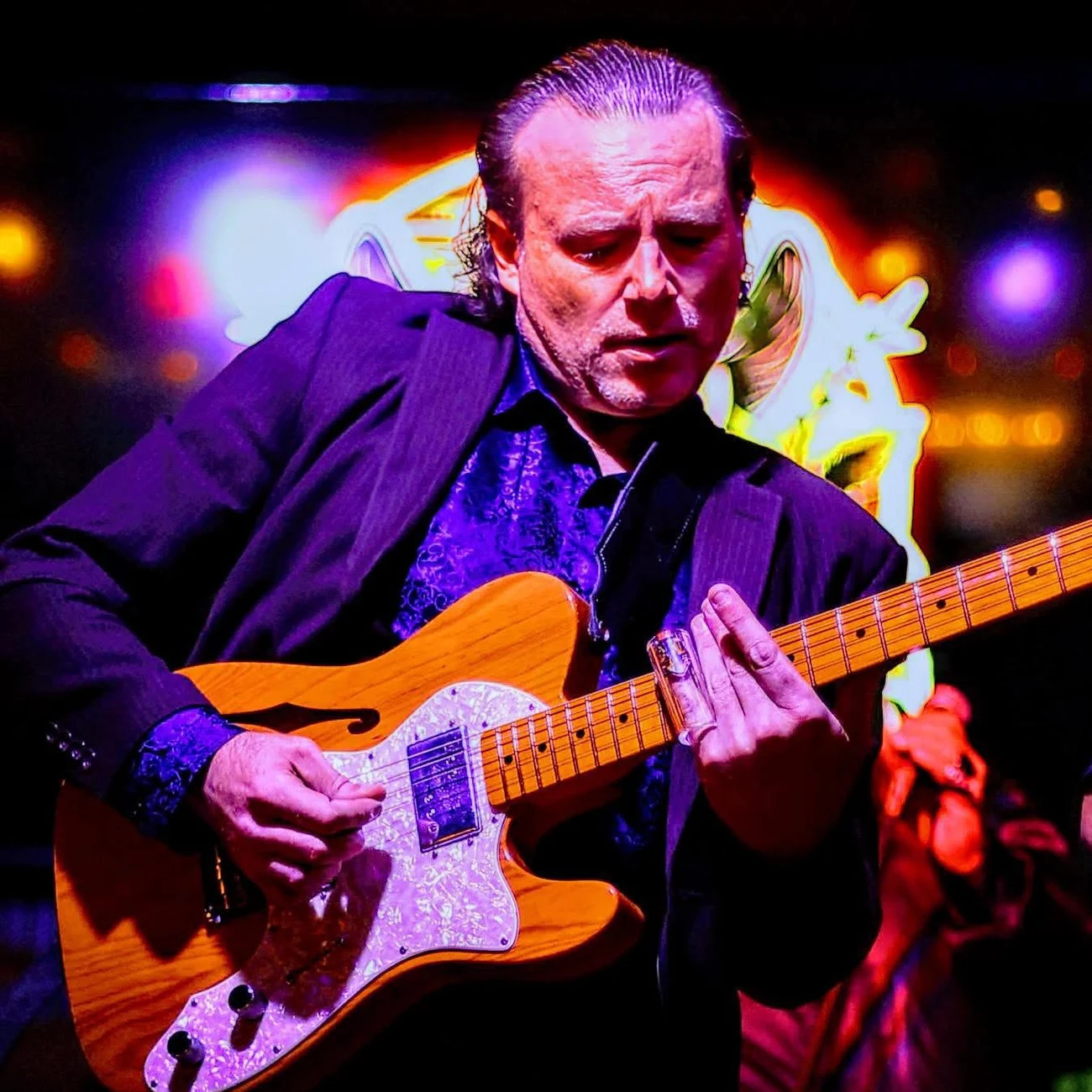 Chris Zemba playing slide guitar under neon stage light
